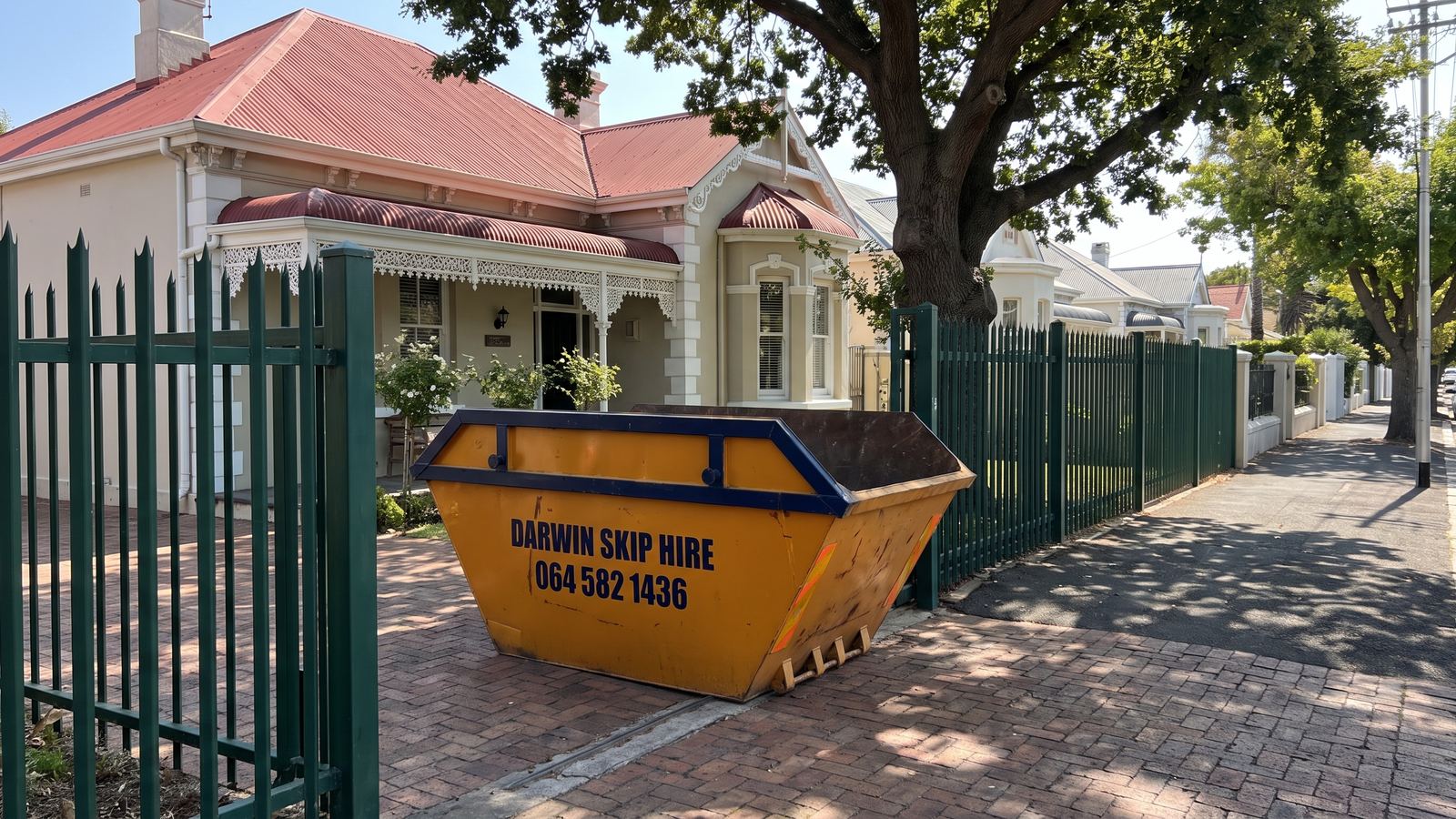 Amber Darwin mini skip inside the open gate of a Victorian semi on an oak-lined street.