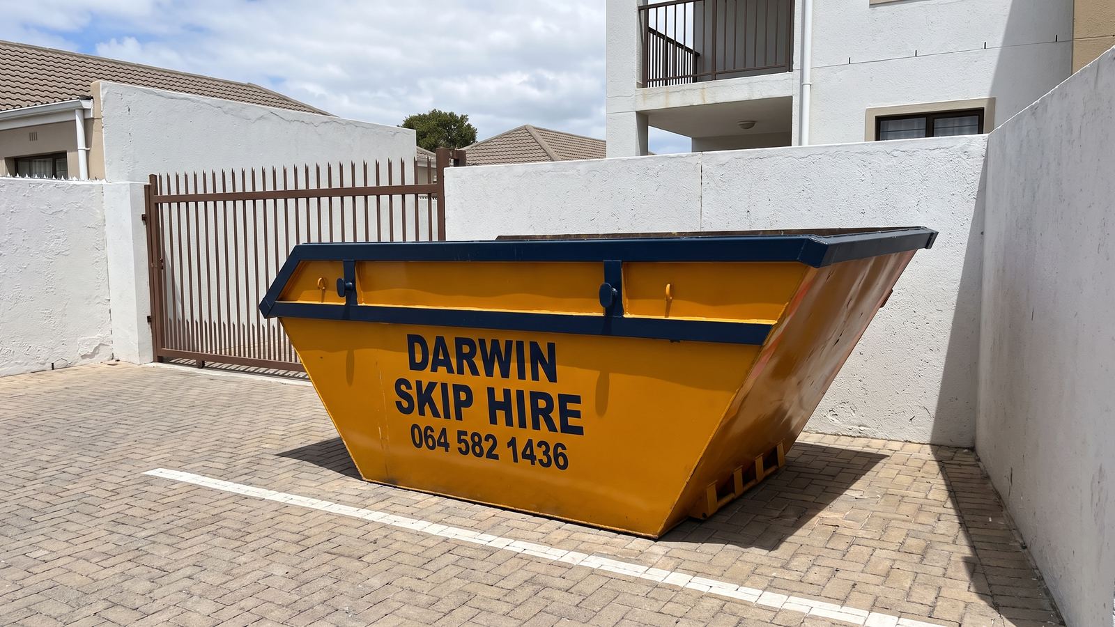 Amber Darwin mini skip in a visitors' bay inside an apartment complex gate.