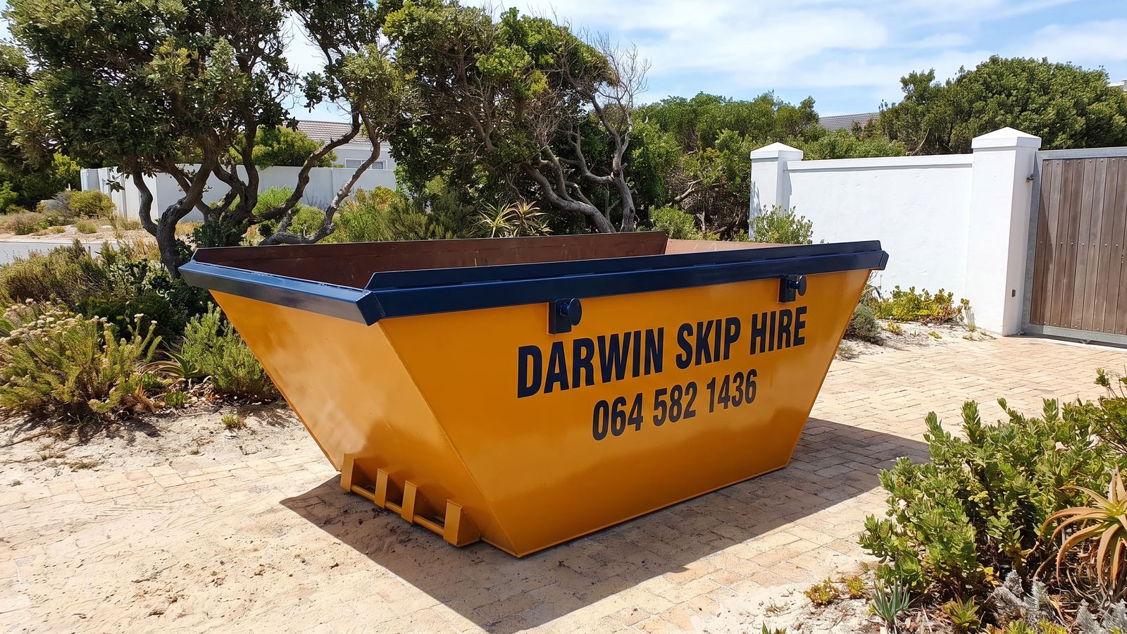 Amber Darwin mini skip on a paved driveway among milkwood trees and fynbos.