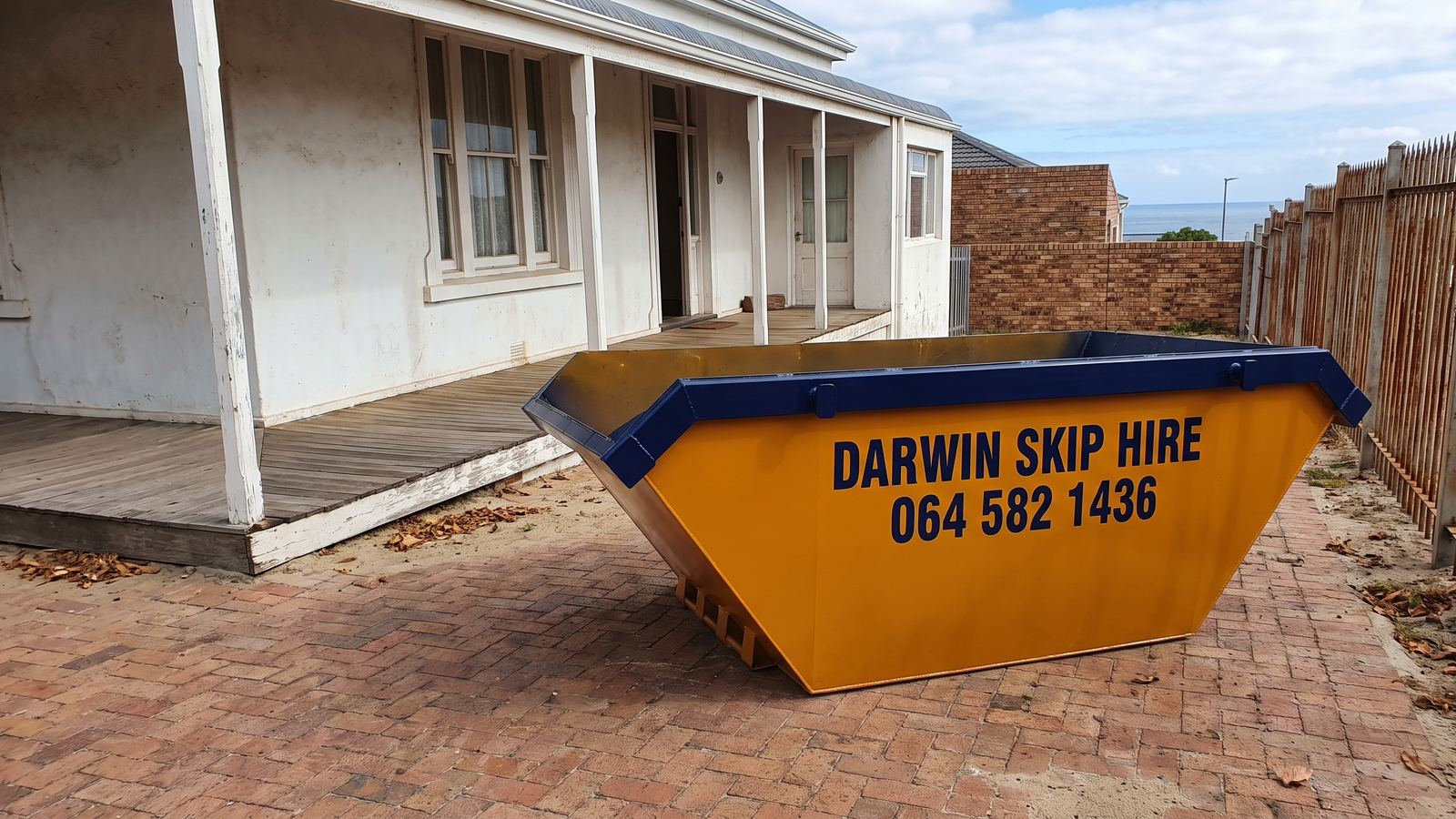 Amber Darwin mini skip on a brick yard beside an old house with a wooden veranda.