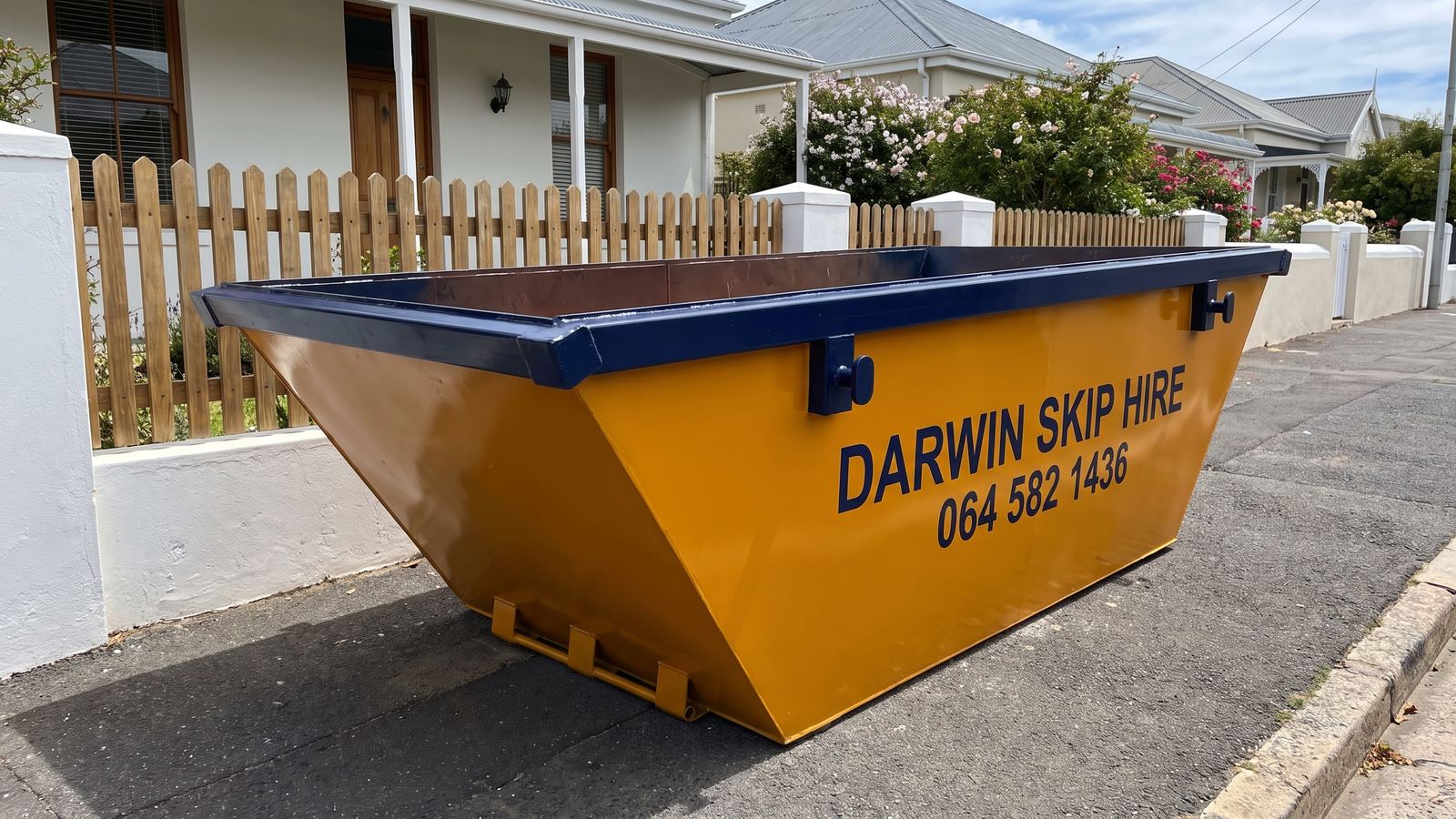 Amber Darwin mini skip beside a picket fence in front of a whitewashed cottage.